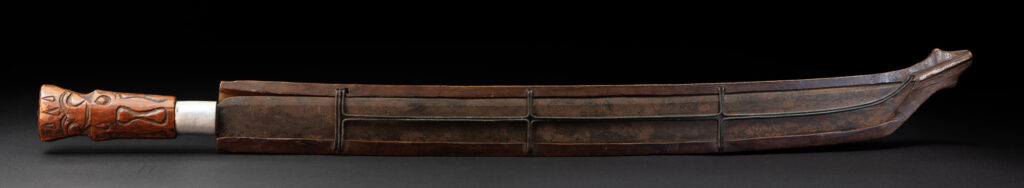 Very fine old sword from the Paiwan tribe, with a scabbard carved with multiple human faces. One side is inlaid with three faience circles.