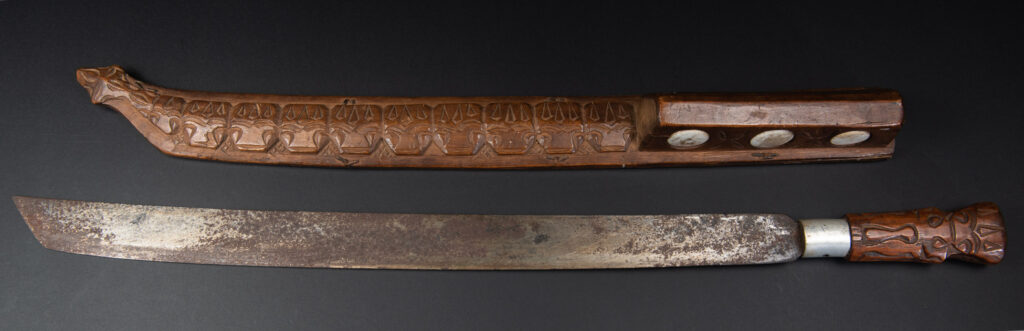 Very fine old sword from the Paiwan tribe, with a scabbard carved with multiple human faces. One side is inlaid with three faience circles.