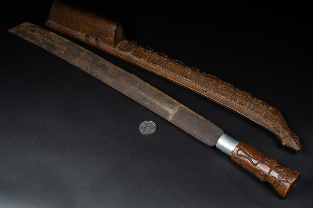 Very fine old sword from the Paiwan tribe, with a scabbard carved with multiple human faces. One side is inlaid with three faience circles.