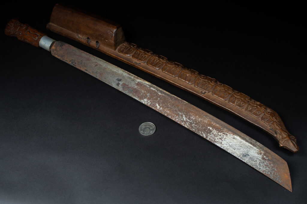 Very fine old sword from the Paiwan tribe, with a scabbard carved with multiple human faces. One side is inlaid with three faience circles.