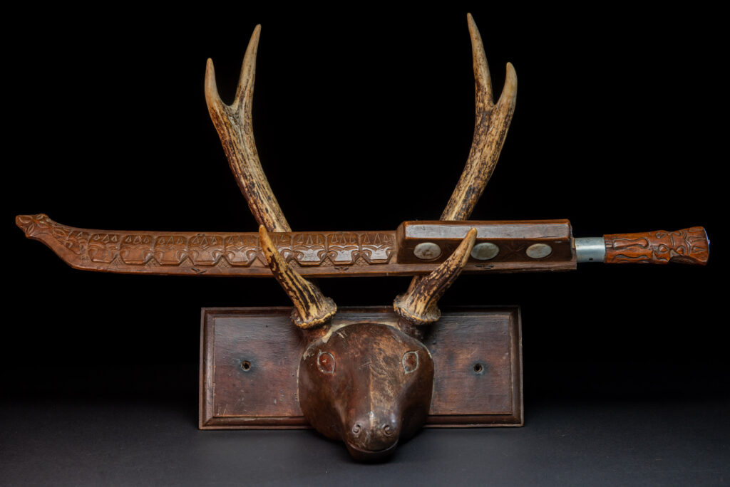 Very fine old sword from the Paiwan tribe, with a scabbard carved with multiple human faces. One side is inlaid with three faience circles.