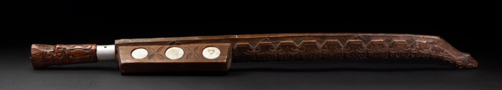 Very fine old sword from the Paiwan tribe, with a scabbard carved with multiple human faces. One side is inlaid with three faience circles.