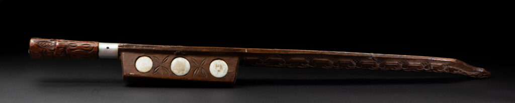 Very fine old sword from the Paiwan tribe, with a scabbard carved with multiple human faces. One side is inlaid with three faience circles.