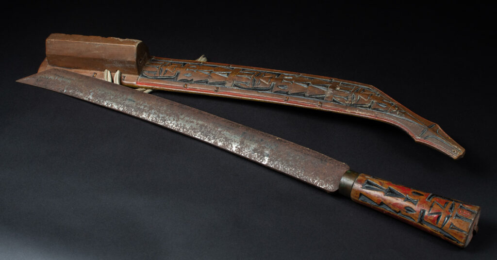 Paiwan tribe sword with a sheath carved with several standing figure and painted in red.