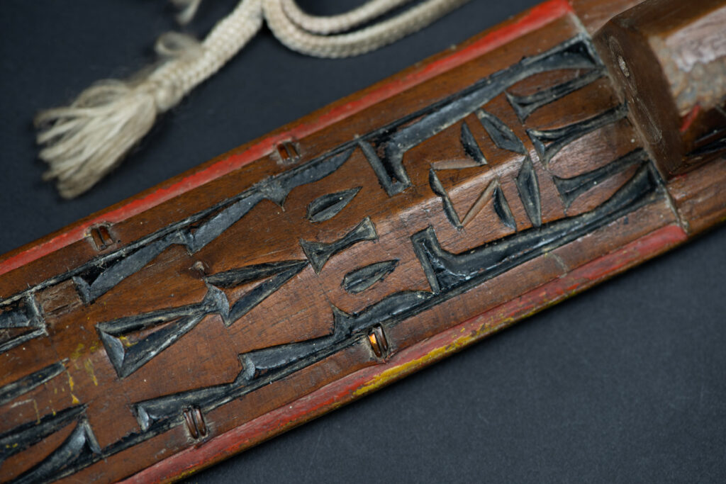 Paiwan tribe sword with a sheath carved with several standing figure and painted in red.