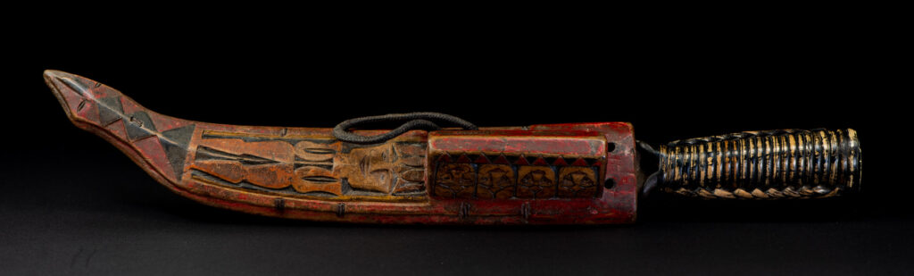 Paiwan tribe hunting knife with a sheath carved with a standing figure and painted in red. The blade and handle are forged as one piece, with the grip wrapped in rattan for protection.