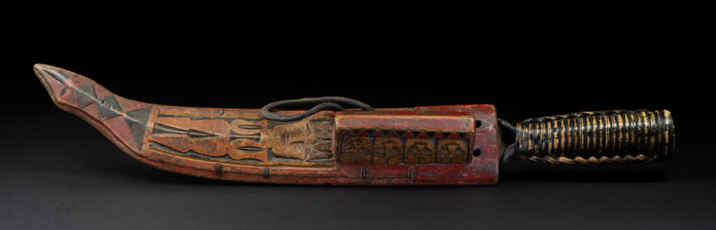 Paiwan tribe hunting knife with a sheath carved with a standing figure and painted in red. The blade and handle are forged as one piece, with the grip wrapped in rattan for protection.