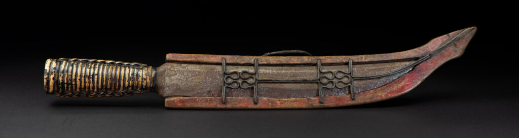 Paiwan tribe hunting knife with a sheath carved with a standing figure and painted in red. The blade and handle are forged as one piece, with the grip wrapped in rattan for protection.