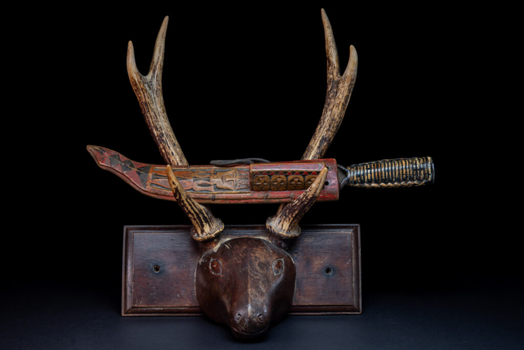 Paiwan tribe hunting knife with a sheath carved with a standing figure and painted in red. The blade and handle are forged as one piece, with the grip wrapped in rattan for protection.