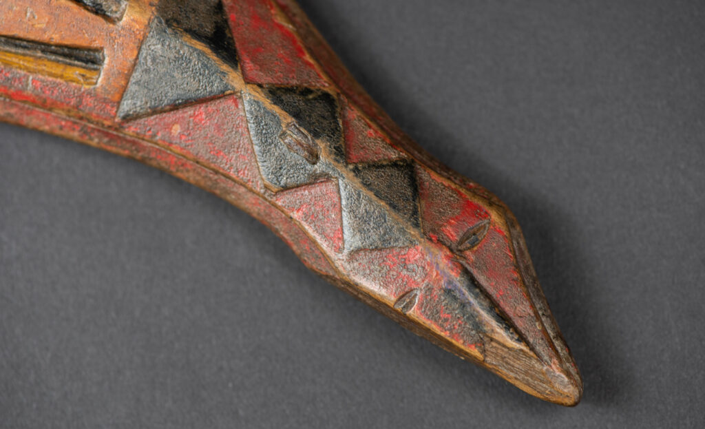 Paiwan tribe hunting knife with a sheath carved with a standing figure and painted in red. The blade and handle are forged as one piece, with the grip wrapped in rattan for protection.