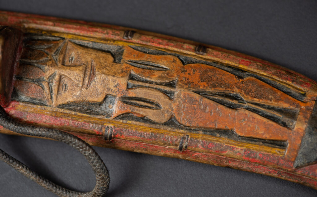Paiwan tribe hunting knife with a sheath carved with a standing figure and painted in red. The blade and handle are forged as one piece, with the grip wrapped in rattan for protection.