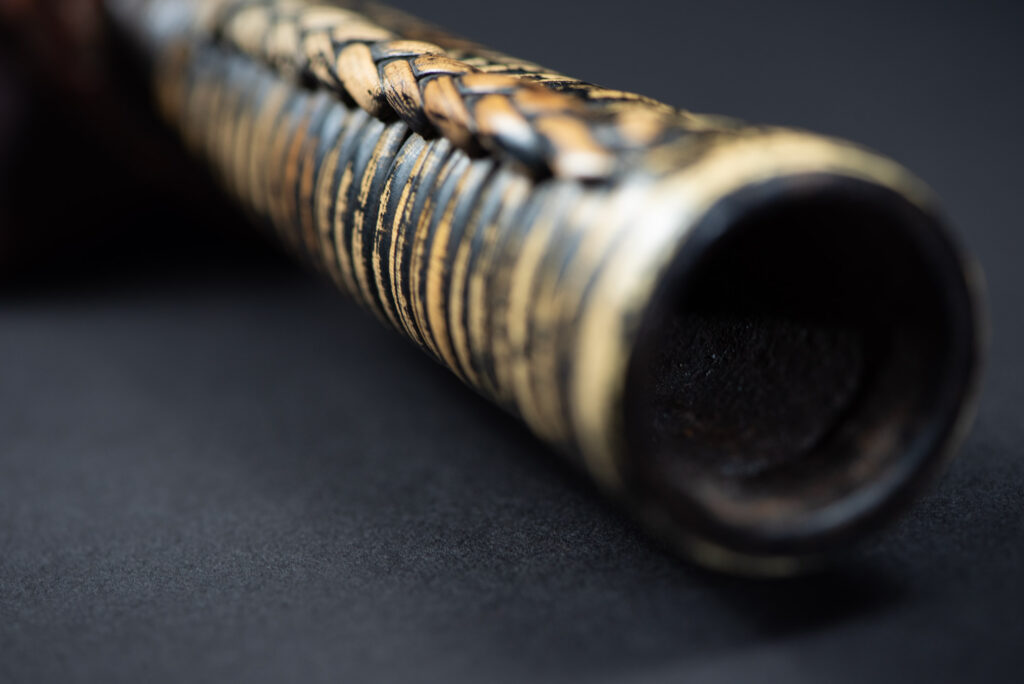 Paiwan tribe hunting knife with a sheath carved with a standing figure and painted in red. The blade and handle are forged as one piece, with the grip wrapped in rattan for protection.