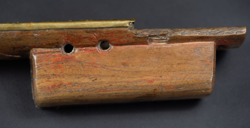 Hunting sword from the Paiwan tribe, with a sheath carved with a scene of a hunter accompanied by his dog shooting at deer. The sides and top of the sheath are covered with brass sheets finely embossed with human head motifs. The sword is made in one piece with the handle, which is wrapped in red-stained rattan.