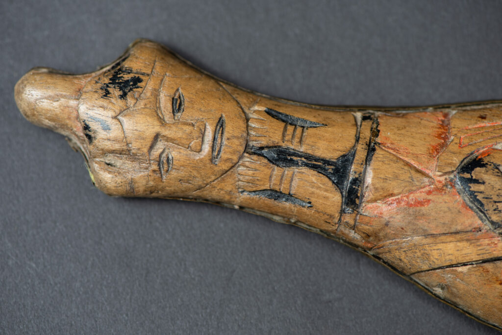 Hunting sword from the Paiwan tribe, with a sheath carved with a scene of a hunter accompanied by his dog shooting at deer. The sides and top of the sheath are covered with brass sheets finely embossed with human head motifs. The sword is made in one piece with the handle, which is wrapped in red-stained rattan.