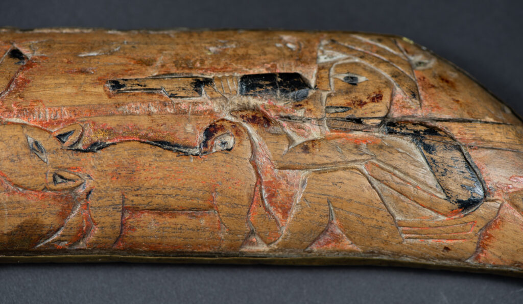 Hunting sword from the Paiwan tribe, with a sheath carved with a scene of a hunter accompanied by his dog shooting at deer. The sides and top of the sheath are covered with brass sheets finely embossed with human head motifs. The sword is made in one piece with the handle, which is wrapped in red-stained rattan.