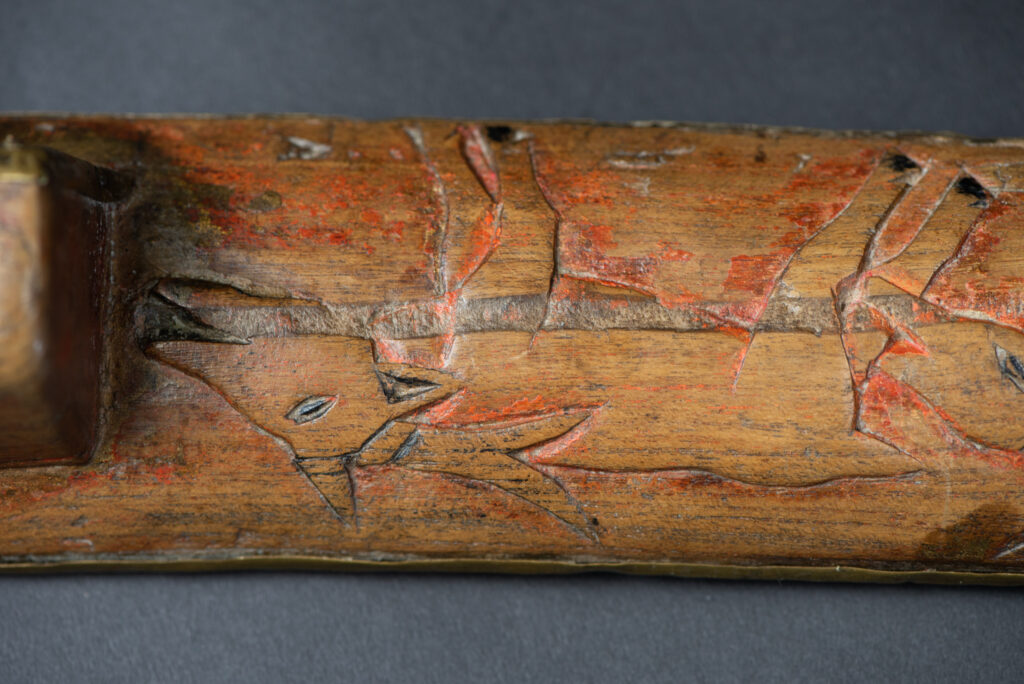 Hunting sword from the Paiwan tribe, with a sheath carved with a scene of a hunter accompanied by his dog shooting at deer. The sides and top of the sheath are covered with brass sheets finely embossed with human head motifs. The sword is made in one piece with the handle, which is wrapped in red-stained rattan.