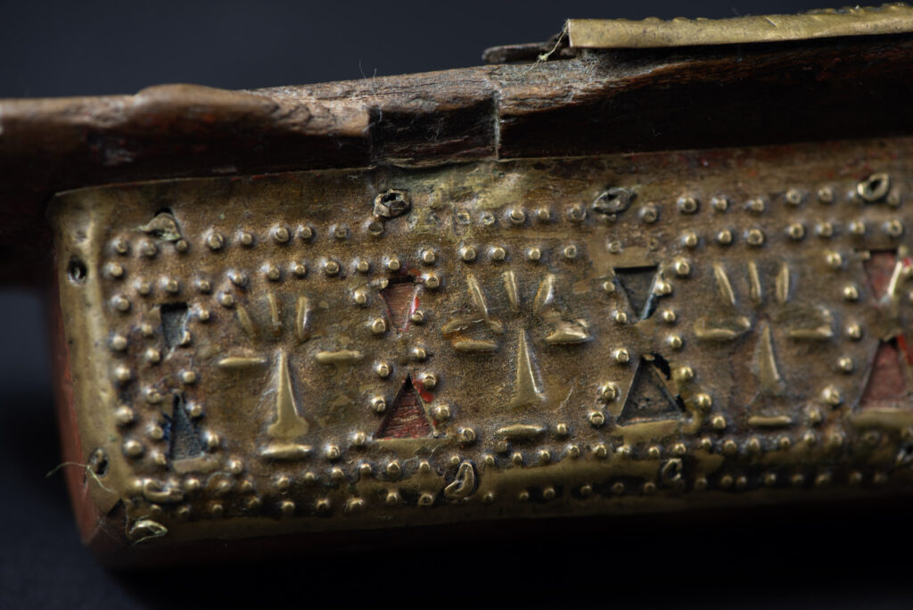Hunting sword from the Paiwan tribe, with a sheath carved with a scene of a hunter accompanied by his dog shooting at deer. The sides and top of the sheath are covered with brass sheets finely embossed with human head motifs. The sword is made in one piece with the handle, which is wrapped in red-stained rattan.