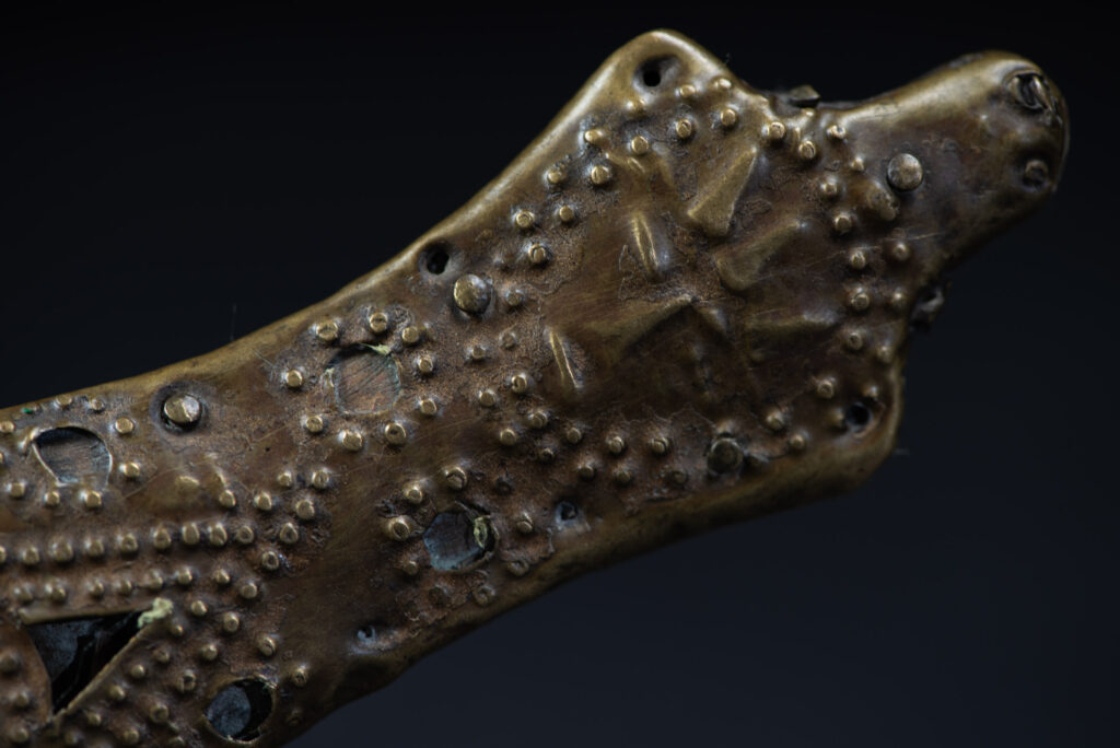 Hunting sword from the Paiwan tribe, with a sheath carved with a scene of a hunter accompanied by his dog shooting at deer. The sides and top of the sheath are covered with brass sheets finely embossed with human head motifs. The sword is made in one piece with the handle, which is wrapped in red-stained rattan.