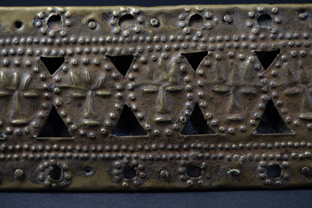 Hunting sword from the Paiwan tribe, with a sheath carved with a scene of a hunter accompanied by his dog shooting at deer. The sides and top of the sheath are covered with brass sheets finely embossed with human head motifs. The sword is made in one piece with the handle, which is wrapped in red-stained rattan.