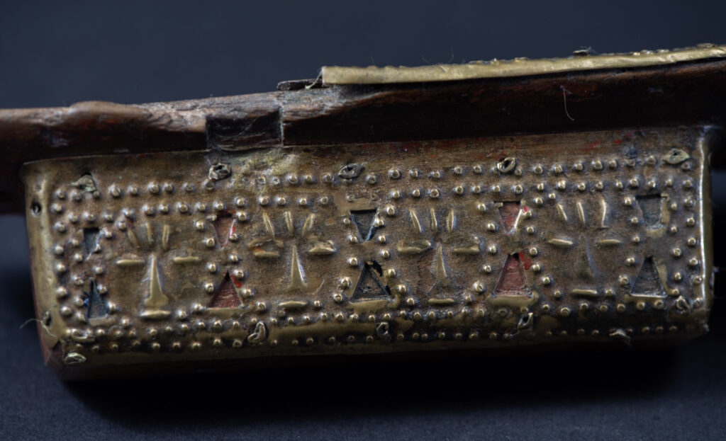 Hunting sword from the Paiwan tribe, with a sheath carved with a scene of a hunter accompanied by his dog shooting at deer. The sides and top of the sheath are covered with brass sheets finely embossed with human head motifs. The sword is made in one piece with the handle, which is wrapped in red-stained rattan.