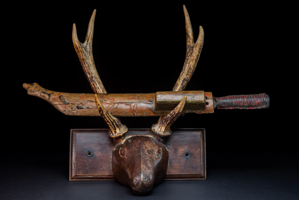 Hunting sword from the Paiwan tribe, with a sheath carved with a scene of a hunter accompanied by his dog shooting at deer. The sides and top of the sheath are covered with brass sheets finely embossed with human head motifs. The sword is made in one piece with the handle, which is wrapped in red-stained rattan.