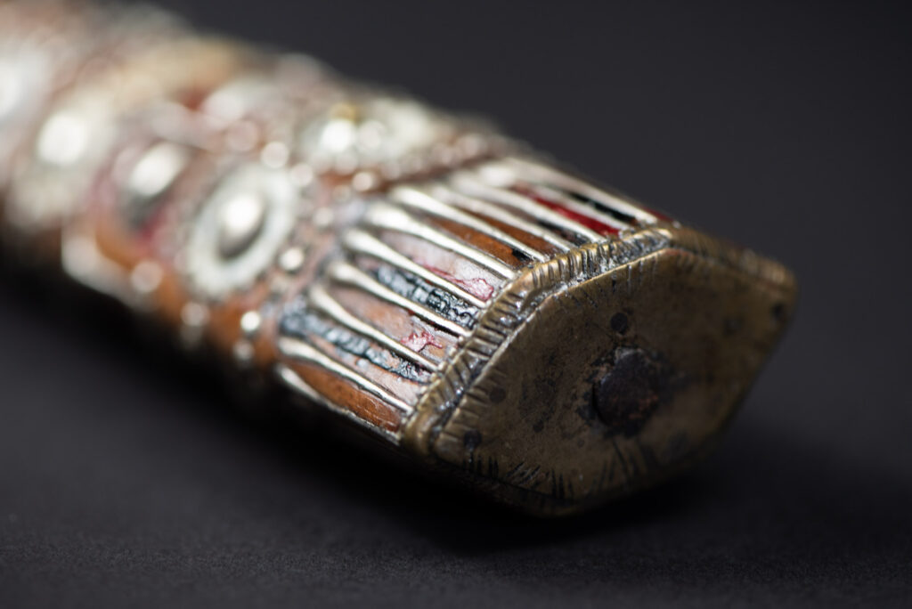 Ancient ceremonial long sword from the Rukai tribe. The back of the sheath is painted red and inlaid with finely engraved snakes in brass sheet. The top is also covered with an engraved brass plate. The very long blade of this Rukai sword features a handle in the Rukai style, decorated with small flower-shaped motifs and aluminum wire. The guard of the sword is made from a Japanese coin.