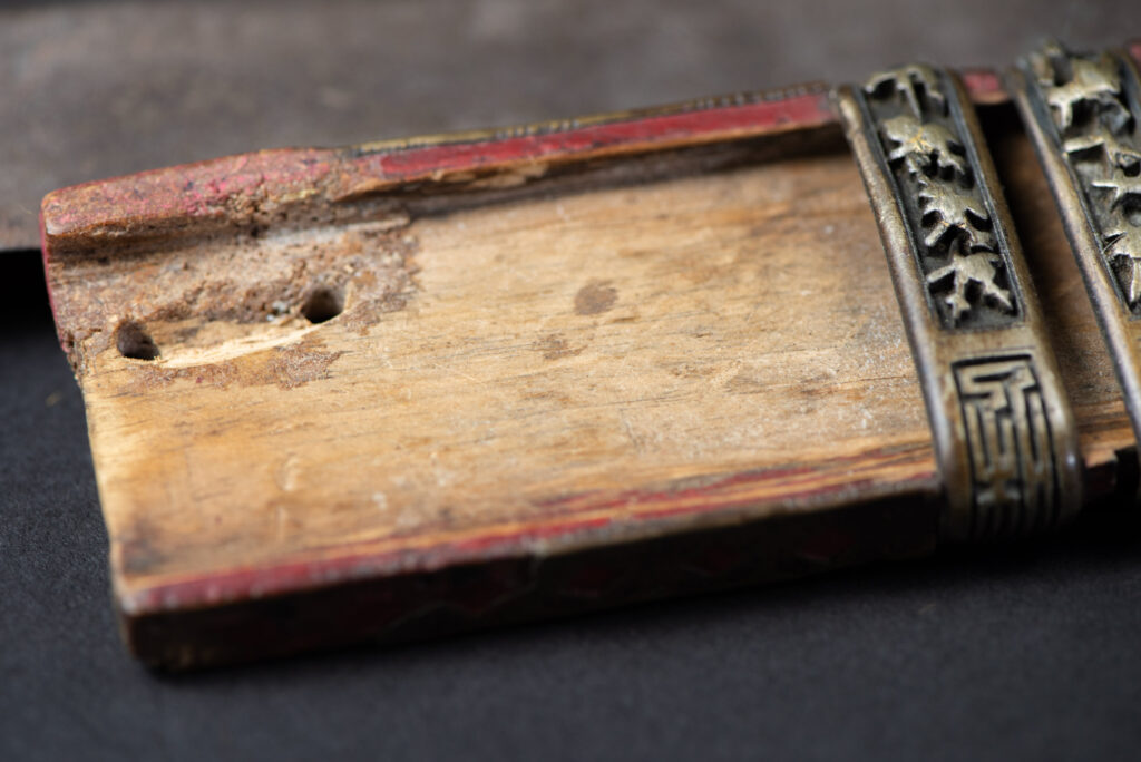 Ancient ceremonial long sword from the Rukai tribe. The back of the sheath is painted red and inlaid with finely engraved snakes in brass sheet. The top is also covered with an engraved brass plate. The very long blade of this Rukai sword features a handle in the Rukai style, decorated with small flower-shaped motifs and aluminum wire. The guard of the sword is made from a Japanese coin..