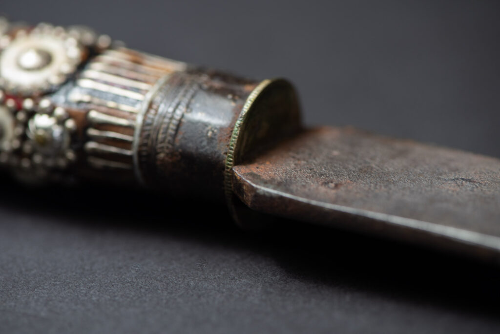 Ancient ceremonial long sword from the Rukai tribe. The back of the sheath is painted red and inlaid with finely engraved snakes in brass sheet. The top is also covered with an engraved brass plate. The very long blade of this Rukai sword features a handle in the Rukai style, decorated with small flower-shaped motifs and aluminum wire. The guard of the sword is made from a Japanese coin.