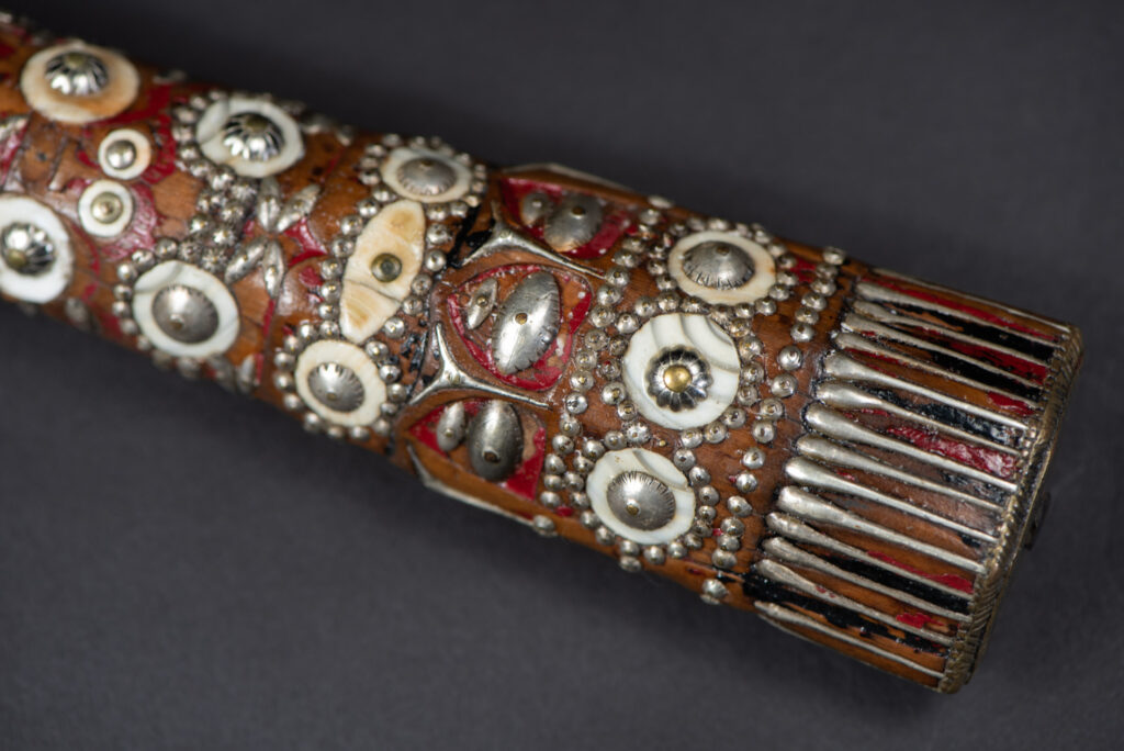 Ancient ceremonial long sword from the Rukai tribe. The back of the sheath is painted red and inlaid with finely engraved snakes in brass sheet. The top is also covered with an engraved brass plate. The very long blade of this Rukai sword features a handle in the Rukai style, decorated with small flower-shaped motifs and aluminum wire. The guard of the sword is made from a Japanese coin.