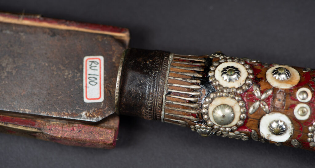 Ancient ceremonial long sword from the Rukai tribe. The back of the sheath is painted red and inlaid with finely engraved snakes in brass sheet. The top is also covered with an engraved brass plate. The very long blade of this Rukai sword features a handle in the Rukai style, decorated with small flower-shaped motifs and aluminum wire. The guard of the sword is made from a Japanese coin.