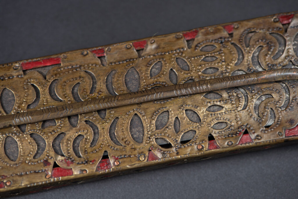 Ancient ceremonial long sword from the Rukai tribe. The back of the sheath is painted red and inlaid with finely engraved snakes in brass sheet. The top is also covered with an engraved brass plate. The very long blade of this Rukai sword features a handle in the Rukai style, decorated with small flower-shaped motifs and aluminum wire. The guard of the sword is made from a Japanese coin.