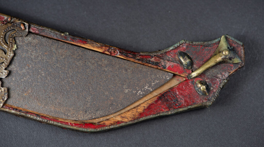 Ancient ceremonial long sword from the Rukai tribe. The back of the sheath is painted red and inlaid with finely engraved snakes in brass sheet. The top is also covered with an engraved brass plate. The very long blade of this Rukai sword features a handle in the Rukai style, decorated with small flower-shaped motifs and aluminum wire. The guard of the sword is made from a Japanese coin.
