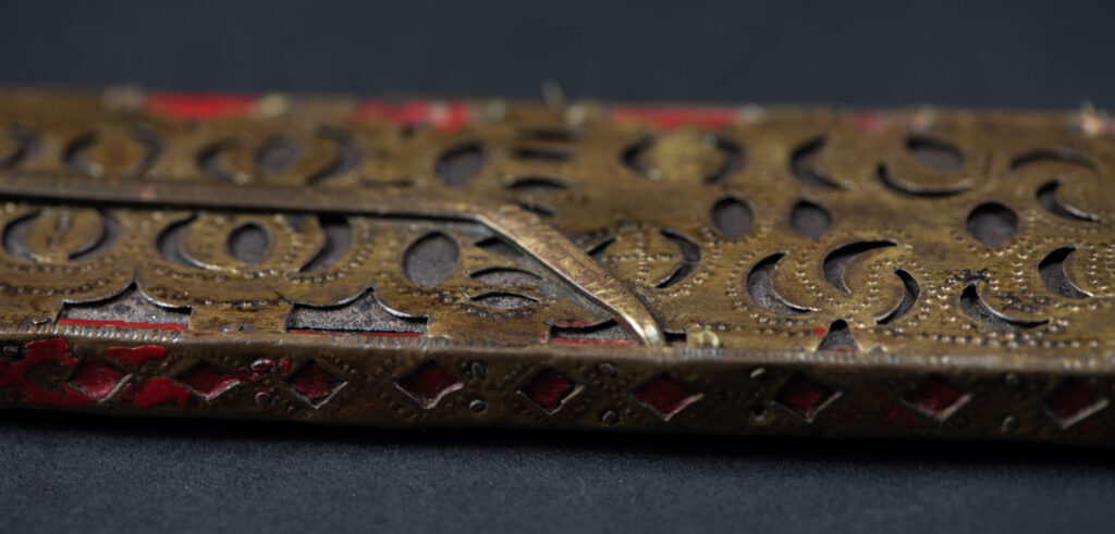 Ancient ceremonial long sword from the Rukai tribe. The back of the sheath is painted red and inlaid with finely engraved snakes in brass sheet. The top is also covered with an engraved brass plate. The very long blade of this Rukai sword features a handle in the Rukai style, decorated with small flower-shaped motifs and aluminum wire. The guard of the sword is made from a Japanese coin.