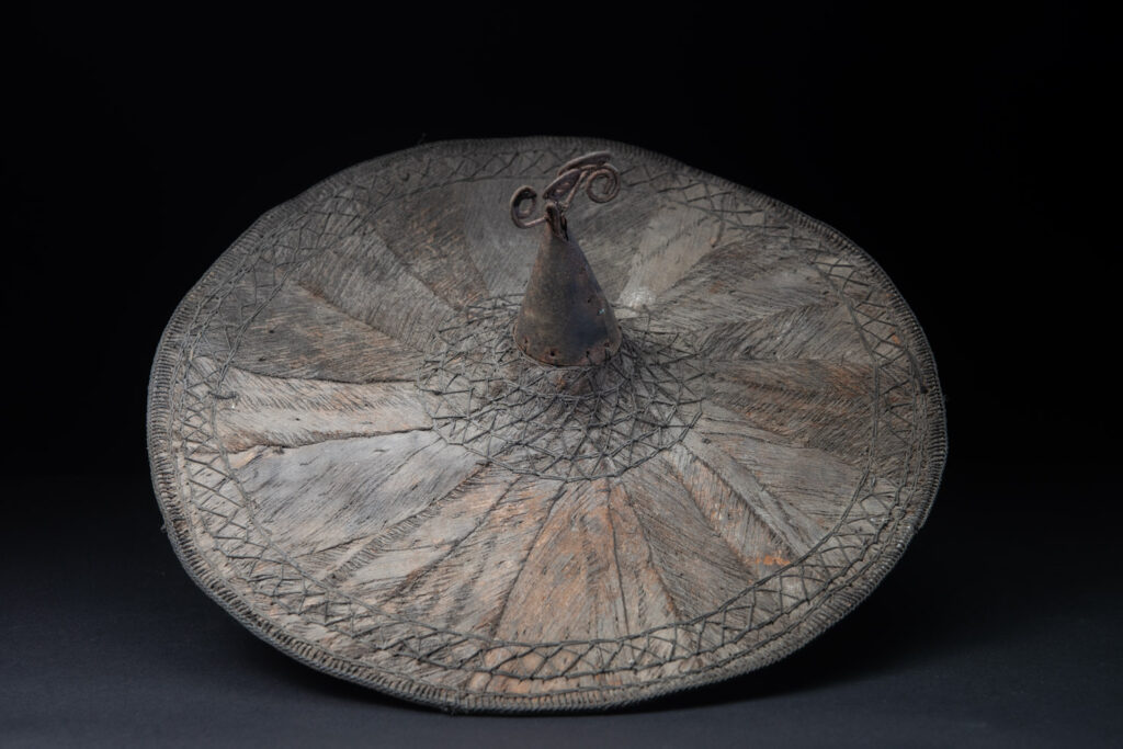 This ancient hat from the Yami- Tao tribes, orchid Island, Taiwan was worn by the female for work in the fields It is named “Varogot”. It is done with coconut palm bark, rotaing, aluminium and iron for the top decoration..