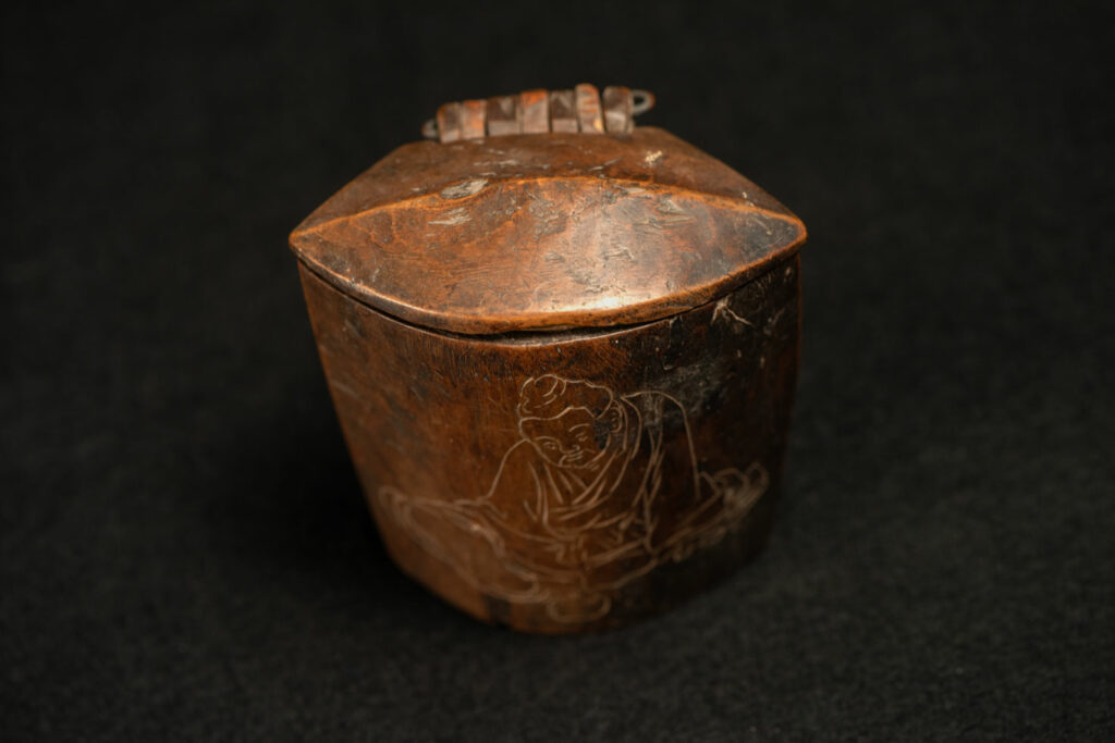 Wooden belt snuffbox from the Pingpu tribes, decorated with an engraving of a Chinese sage. It features a hinged lid carved from a single piece of wood and a section designed for attachment to the belt.