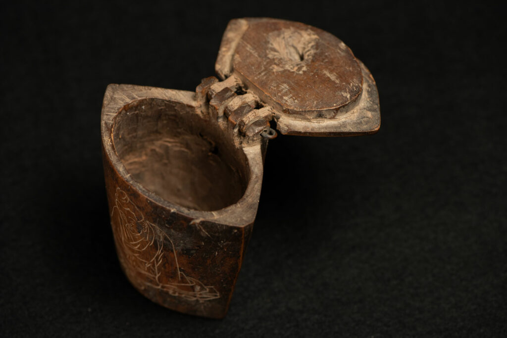 Wooden belt snuffbox from the Pingpu tribes, decorated with an engraving of a Chinese sage. It features a hinged lid carved from a single piece of wood and a section designed for attachment to the belt.