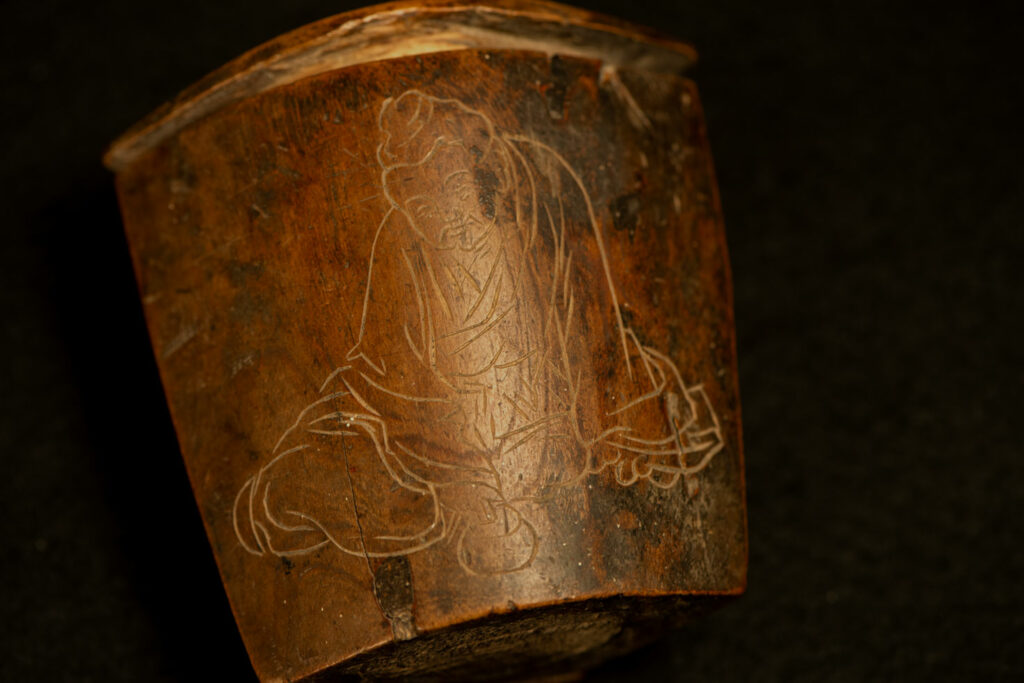 Wooden belt snuffbox from the Pingpu tribes, decorated with an engraving of a Chinese sage. It features a hinged lid carved from a single piece of wood and a section designed for attachment to the belt.