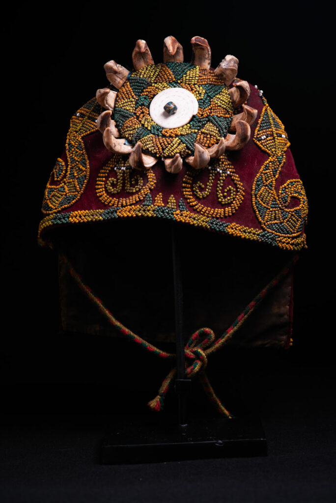 Paiwan tribe: ceremonial men's hat made of velvet, adorned with beadwork forming sacred snakes, and featuring a central rosette decorated with a round shell and boar tusks.