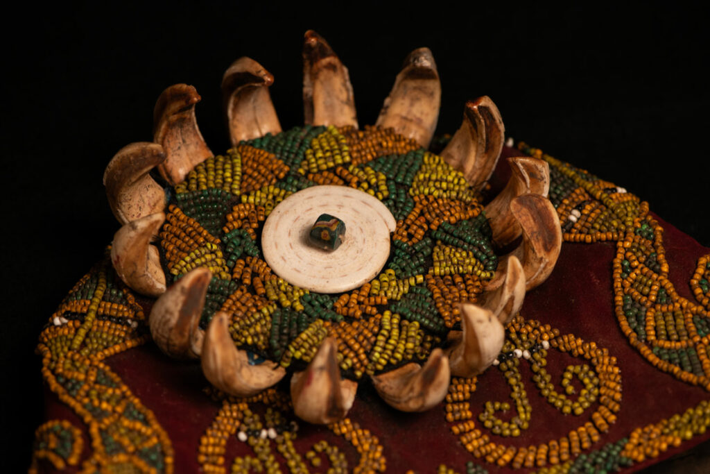 Paiwan tribe: ceremonial men's hat made of velvet, adorned with beadwork forming sacred snakes, and featuring a central rosette decorated with a round shell and boar tusks.