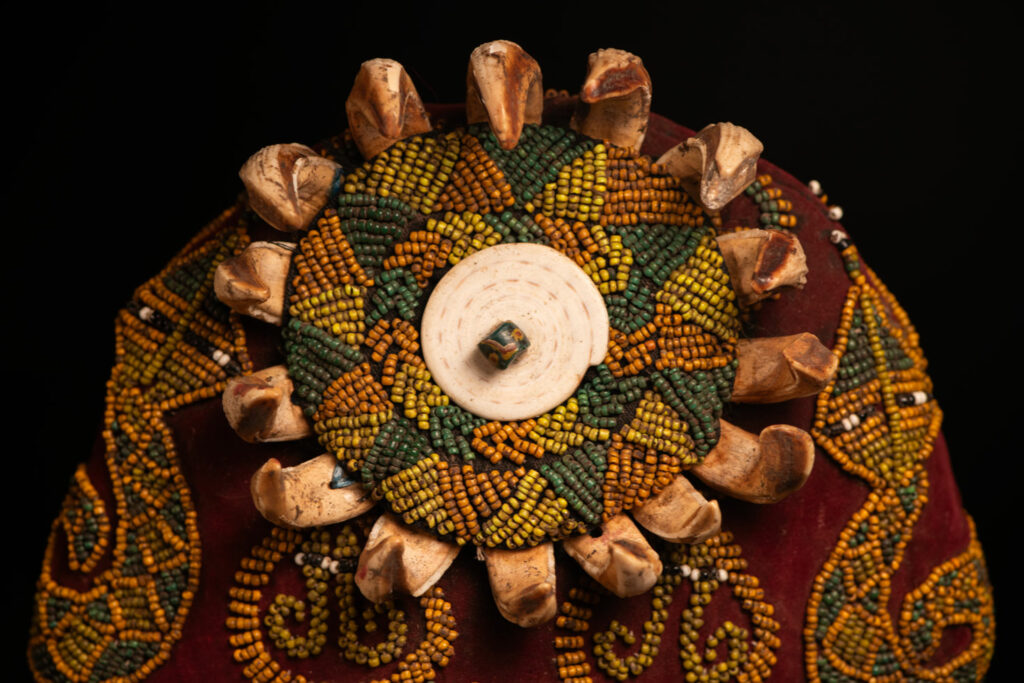 Paiwan tribe: ceremonial men's hat made of velvet, adorned with beadwork forming sacred snakes, and featuring a central rosette decorated with a round shell and boar tusks.