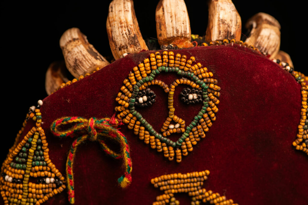 Paiwan tribe: ceremonial men's hat made of velvet, adorned with beadwork forming sacred snakes, and featuring a central rosette decorated with a round shell and boar tusks.