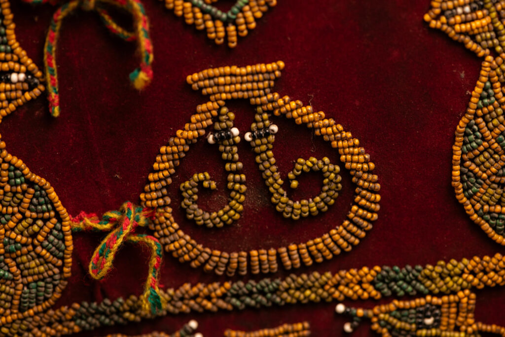 Paiwan tribe: ceremonial men's hat made of velvet, adorned with beadwork forming sacred snakes, and featuring a central rosette decorated with a round shell and boar tusks.
