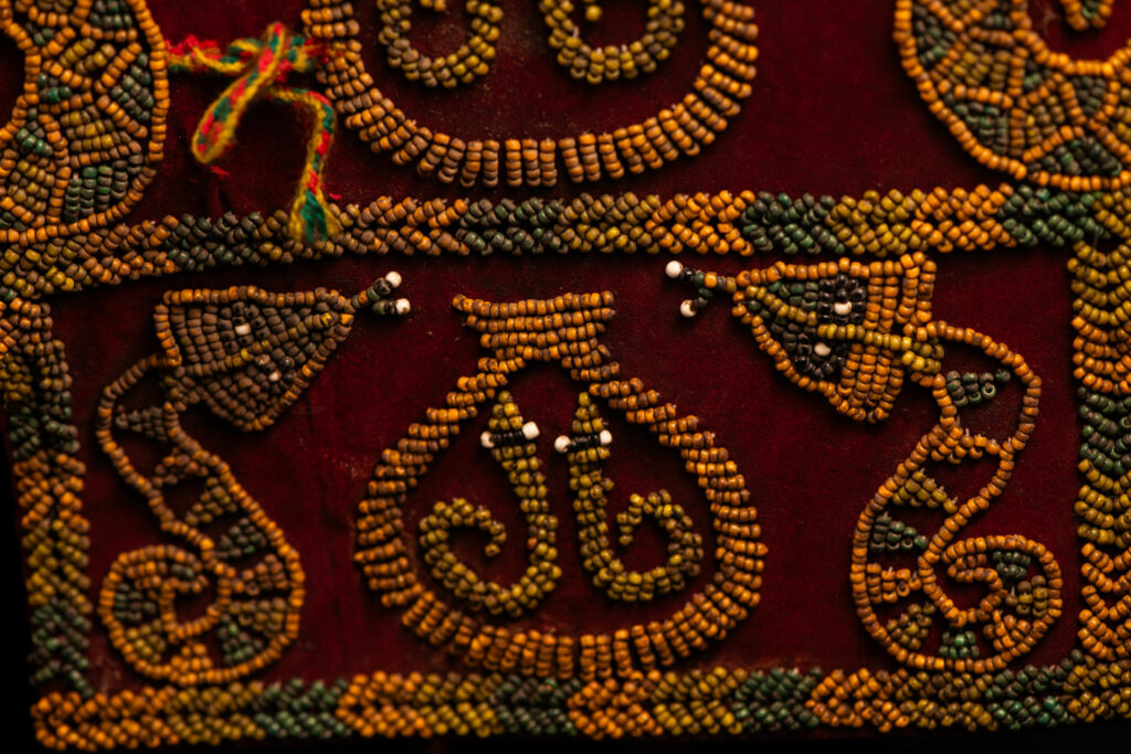 Paiwan tribe: ceremonial men's hat made of velvet, adorned with beadwork forming sacred snakes, and featuring a central rosette decorated with a round shell and boar tusks.
