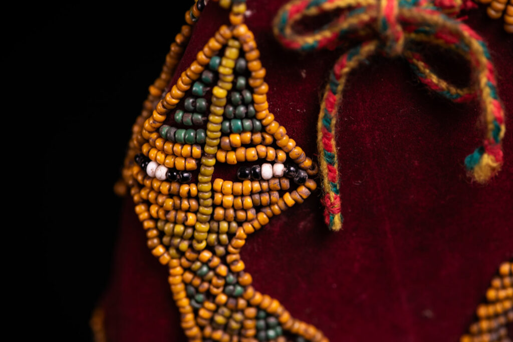 Paiwan tribe: ceremonial men's hat made of velvet, adorned with beadwork forming sacred snakes, and featuring a central rosette decorated with a round shell and boar tusks.