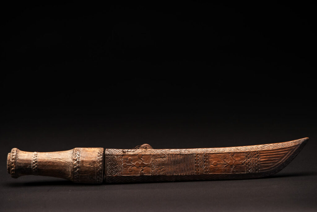 ‘Ipagan’ Knife and its sheath from the Yami (Tao) tribe. A fine example of the “Ipagan”, a short sword used to exorcise evil spirits but also to harvest. This sword, shorter than the Pararowai model, is notable for having both its handle and sheath carved with wave patterns, triangles, and the figure of the god Magamaog.