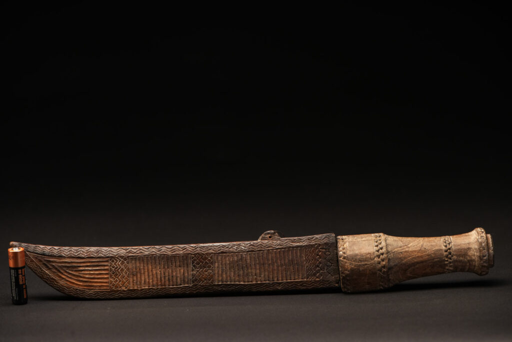 ‘Ipagan’ Knife and its sheath from the Yami (Tao) tribe. A fine example of the “Ipagan”, a short sword used to exorcise evil spirits but also to harvest. This sword, shorter than the Pararowai model, is notable for having both its handle and sheath carved with wave patterns, triangles, and the figure of the god Magamaog.