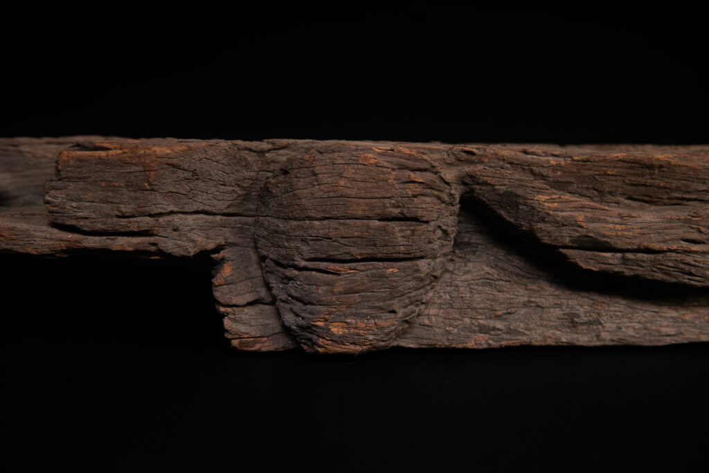 19th-century door lintel from the Paiwan tribe, carved with a pair of snakes facing each other and two human faces on either side. This Paiwan panel is heavily eroded and was probably placed above the entrance, exposed to the elements.