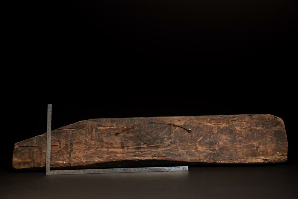 19th-century door lintel from the Paiwan tribe, carved with human heads topped by sacred snakes, along with two standing figures, likely a couple. This Paiwan lintel is painted in black, red, and yellow.