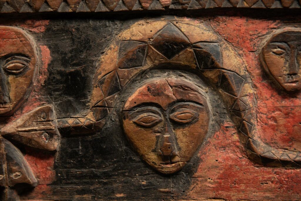 19th-century door lintel from the Paiwan tribe, carved with human heads topped by sacred snakes, along with two standing figures, likely a couple. This Paiwan lintel is painted in black, red, and yellow.