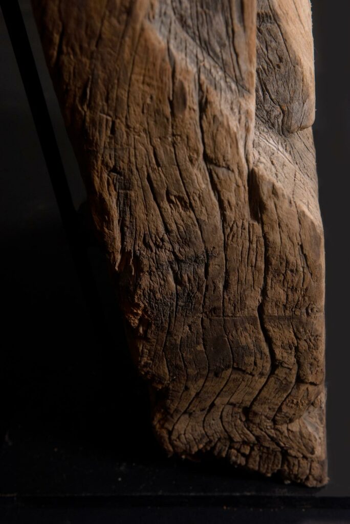 Paiwan tribe: massive 19th-century ancestral panel measuring over 2.5 meters, depicting a hunter wearing a Paiwan-style hat and holding a knife and a spear at his side. The carvings on his torso suggest he is dressed in a ceremonial vest and the shoulder belt traditionally worn by nobles. Due to its size, this panel was likely the central piece of the house.